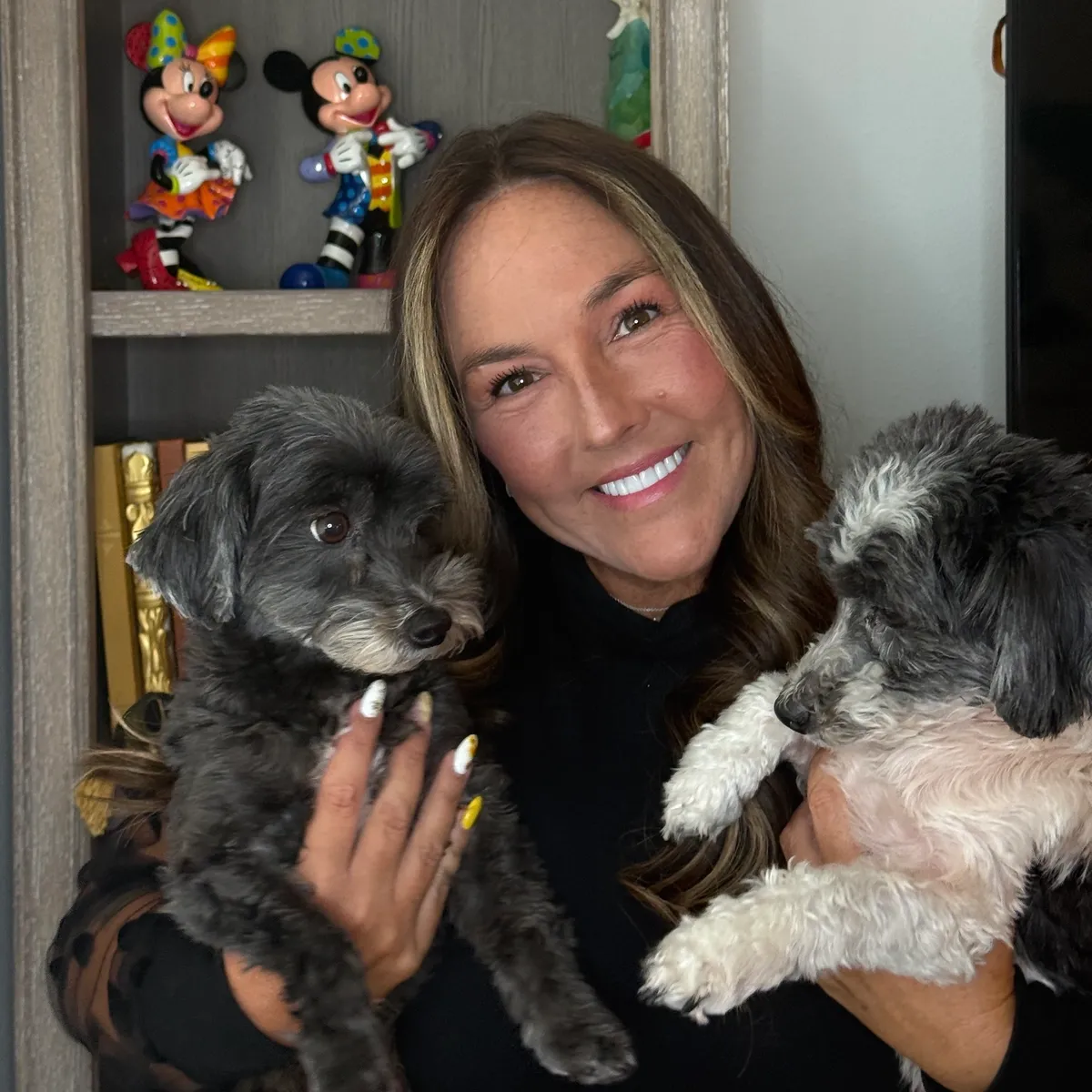 Woman smiling while holding two small dogs indoors.
