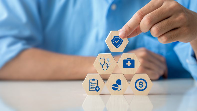 Hand stacking wooden blocks with healthcare icons, symbolizing medical services.